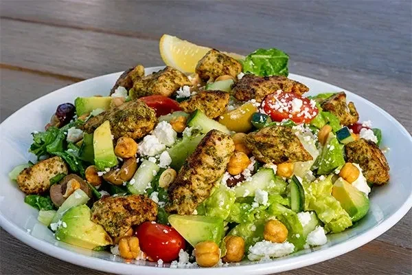 Grilled chicken salad with lettuce, tomatoes, avocado, feta, and lemon.