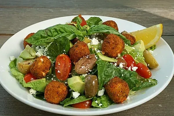 Fresh salad with lettuce, crispy balls, tomatoes, avocado, olives, and feta.
