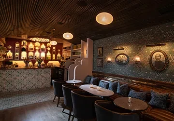 Dimly lit, stylish bar lounge with patterned counter and framed portraits.