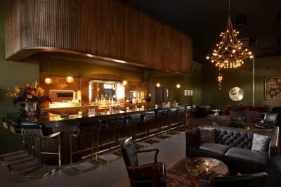Empty, elegant bar and lounge with dark leather seating and chandelier.