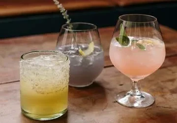 Three distinct, garnished cocktails with ice on a wooden surface.