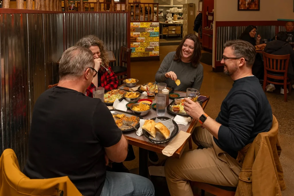 Four smiling people dining and conversing in a restaurant.