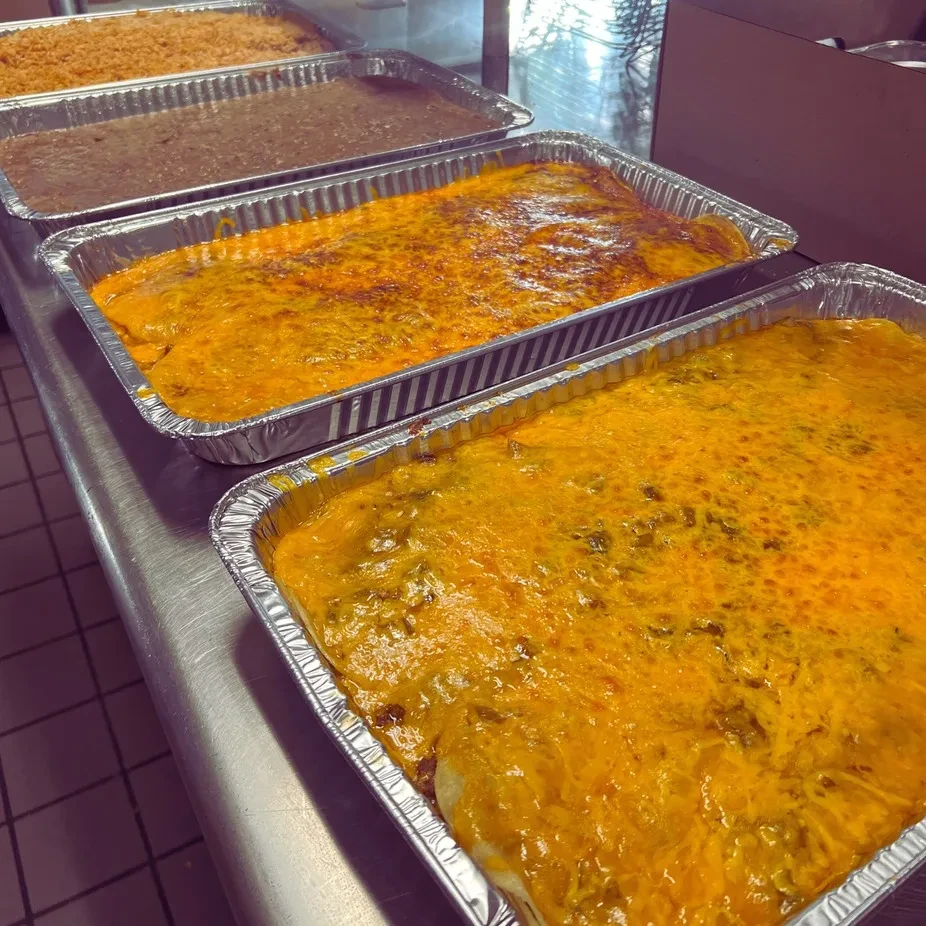 Four large foil pans of cheesy casserole, refried beans, and rice.