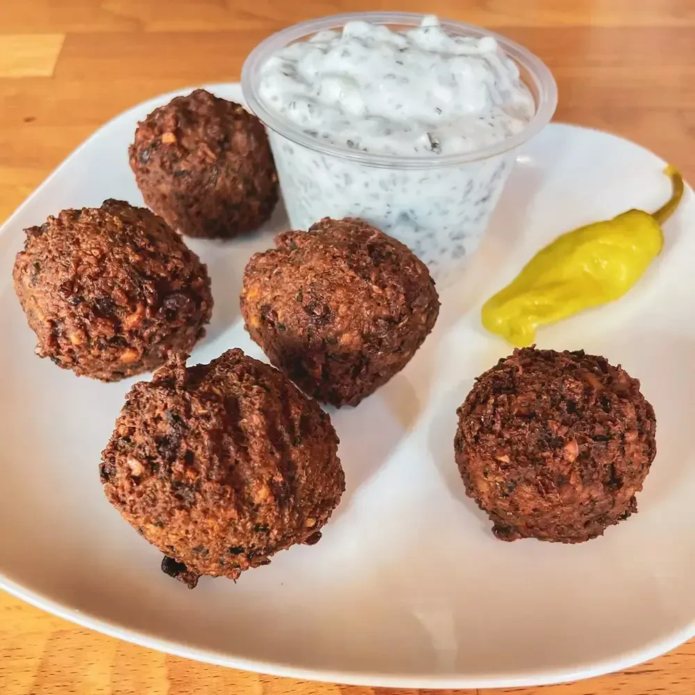 Five deep-fried falafel, sauce, and a pickled pepper on a white plate.
