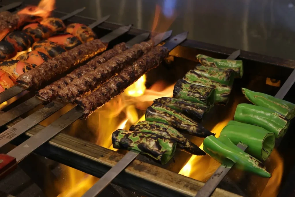 Skewers of meat, tomato, and pepper kebabs grilling over flames.