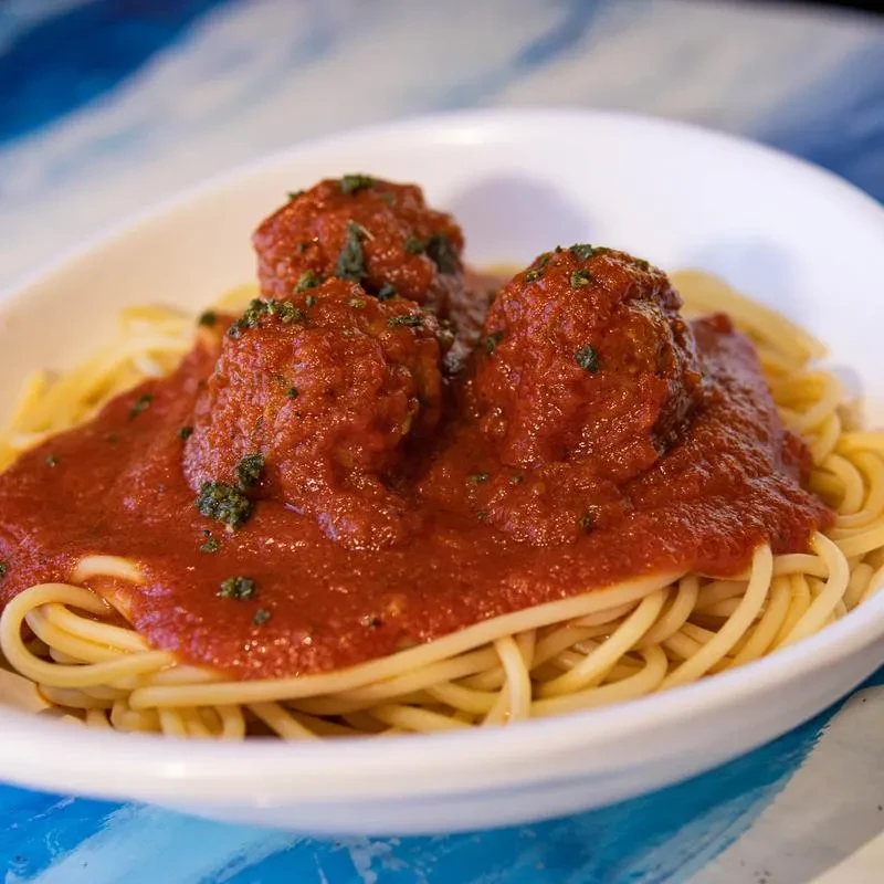 Close-up: spaghetti and three meatballs with red sauce and herbs.