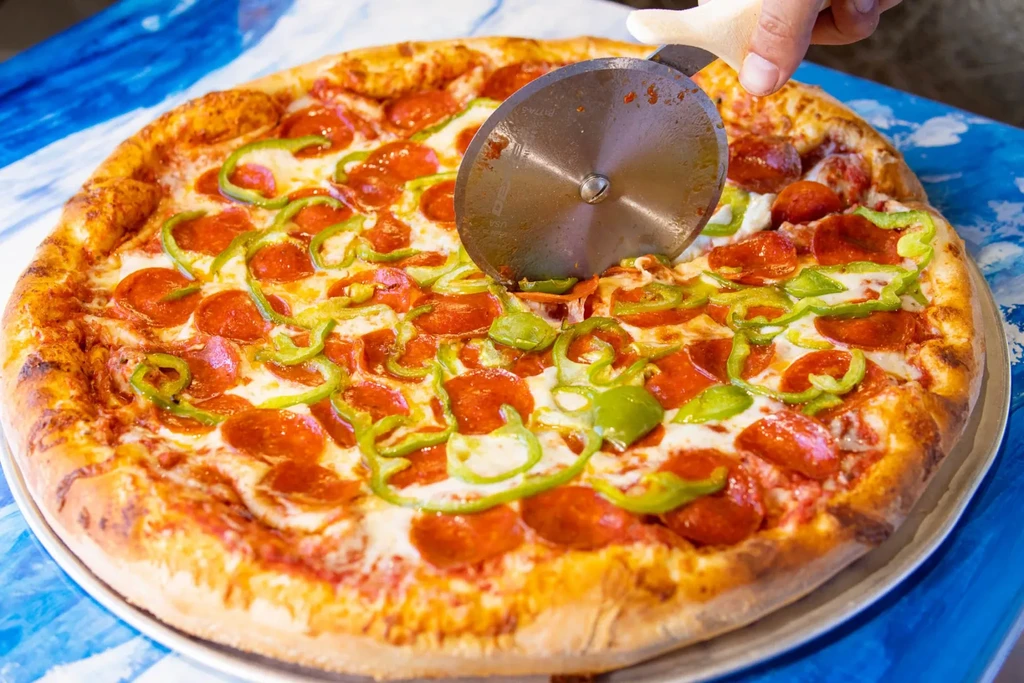 Hand cutting pepperoni and green bell pepper pizza.