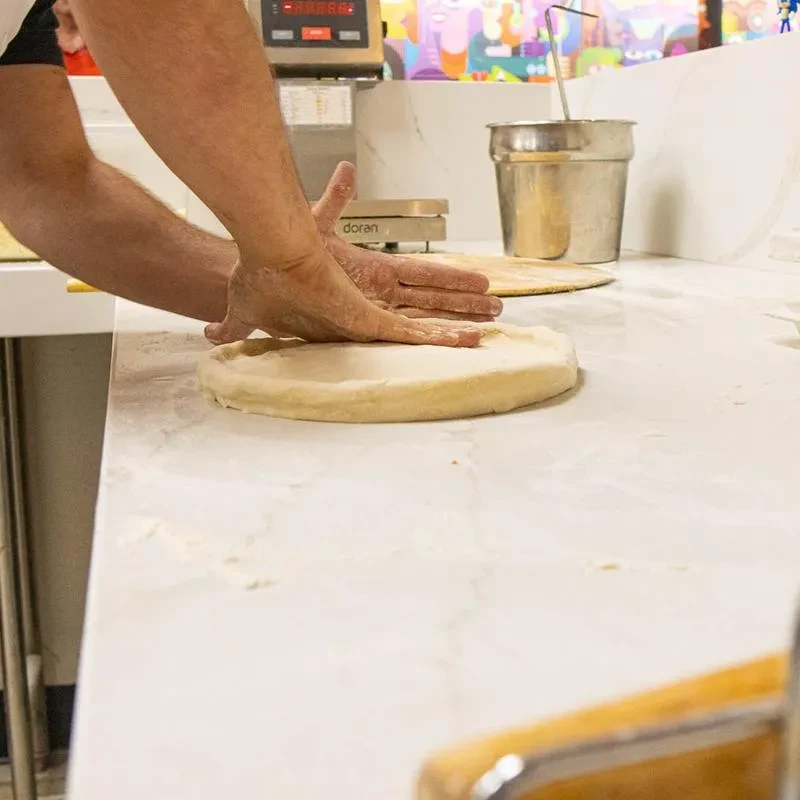 Close-up of hands pressing pizza dough on a floured counter.