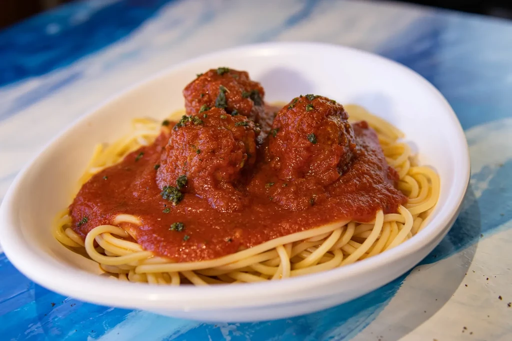 Spaghetti and meatballs with marinara sauce and herbs in a white bowl.