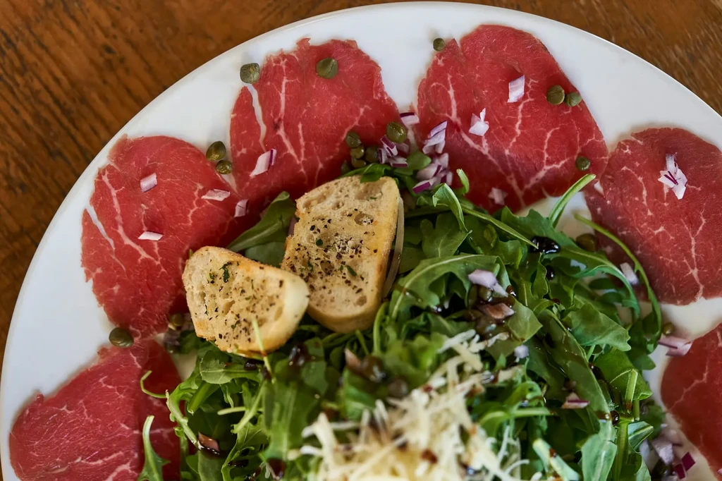 Close-up of beef carpaccio with arugula, capers, parmesan, and crusty bread.
