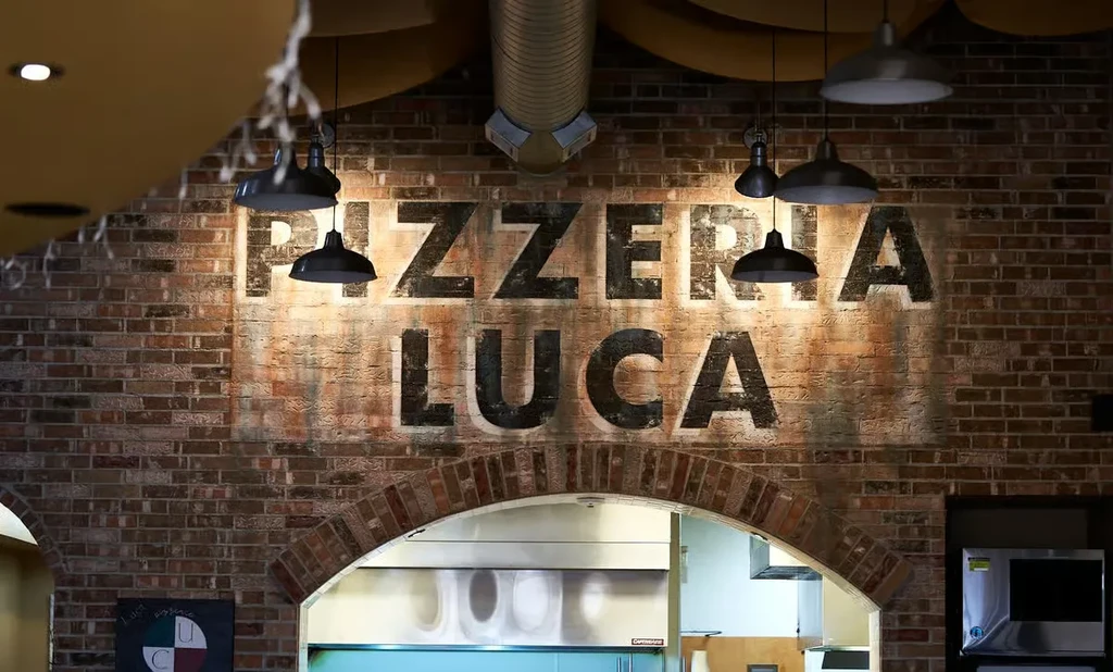 Rustic brick wall with Pizzeria Luca sign, industrial lights, kitchen view.