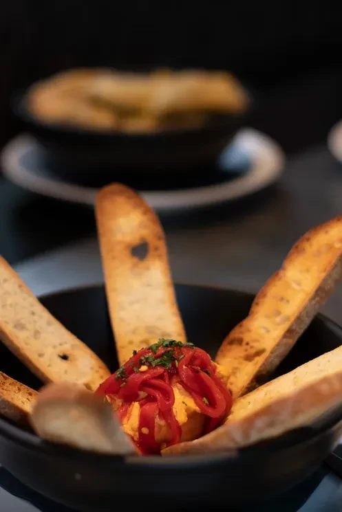Creamy dip with red peppers and herbs, surrounded by toasted baguette.