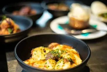 Creamy pasta with green herbs in black bowl, other dishes blurred.