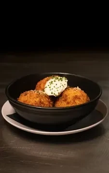 Three crispy fried golden spheres with creamy sauce and green herbs.