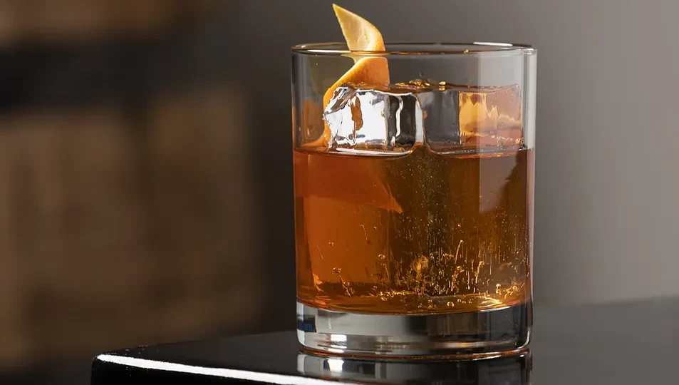 Amber cocktail with ice and citrus peel in a rocks glass.