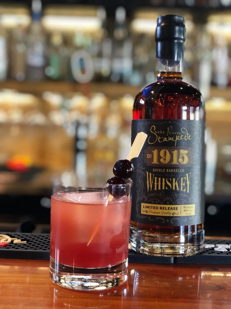 Whiskey bottle and cherry cocktail on a wooden bar.