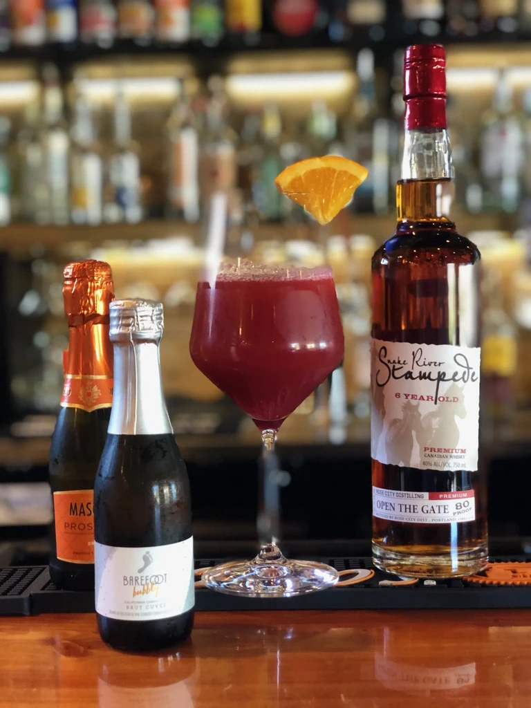 Red cocktail, whisky, and two sparkling wines on a dark wooden bar.