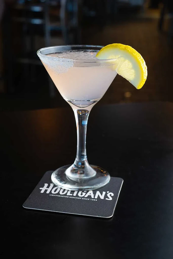 Pink cocktail in martini glass with lemon garnish on 'HOOLIGAN'S' coaster.