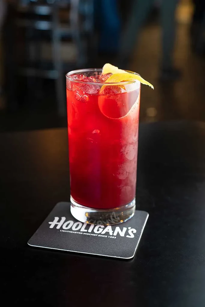 A red cocktail with lemon peel and ice on a "HOOLIGAN'S" coaster.
