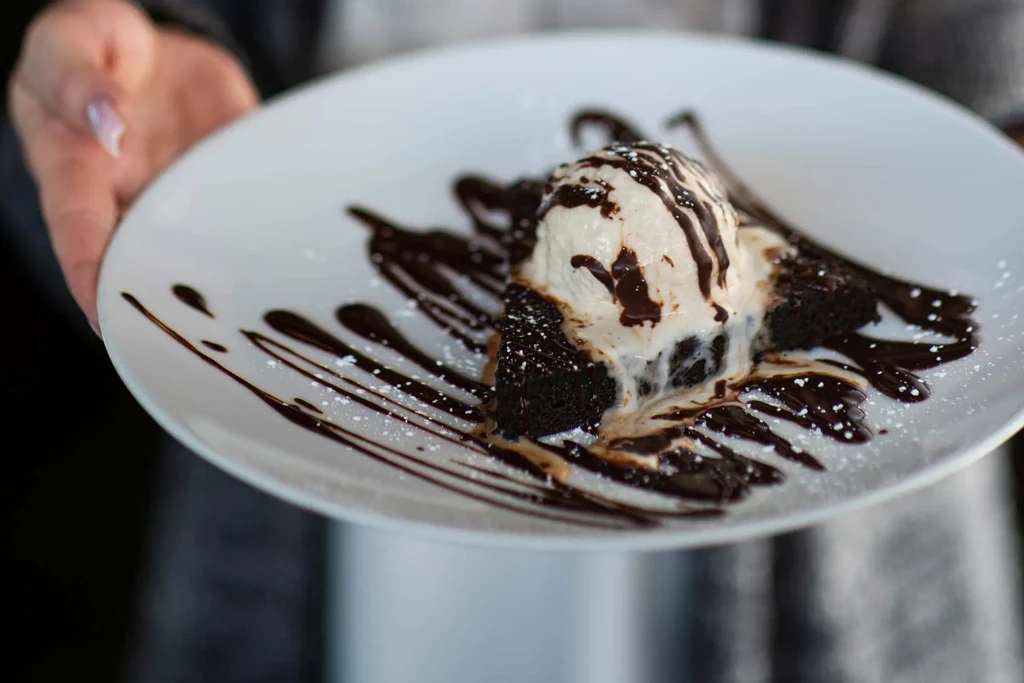Chocolate brownie with melting vanilla ice cream, chocolate sauce, and powdered sugar.