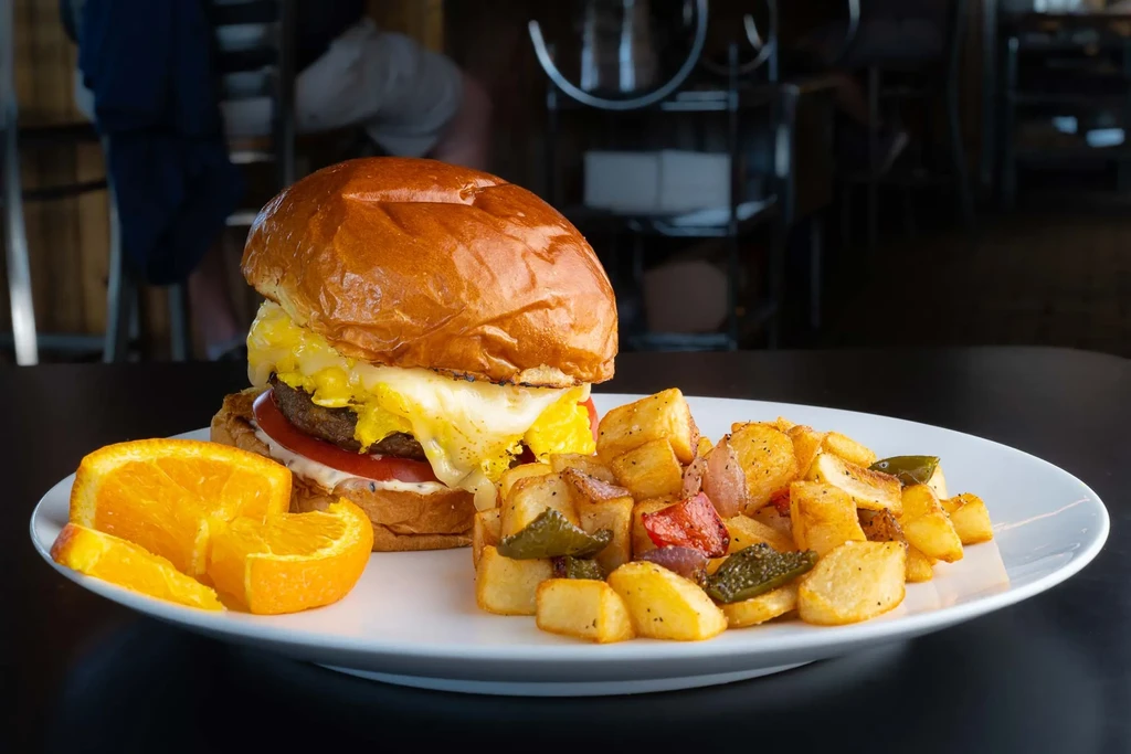 Breakfast burger with egg, home fries, and orange slices on a plate.