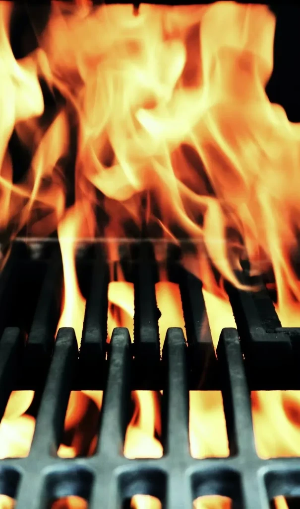 Intense orange flames engulfing dark metal grill grates from below.