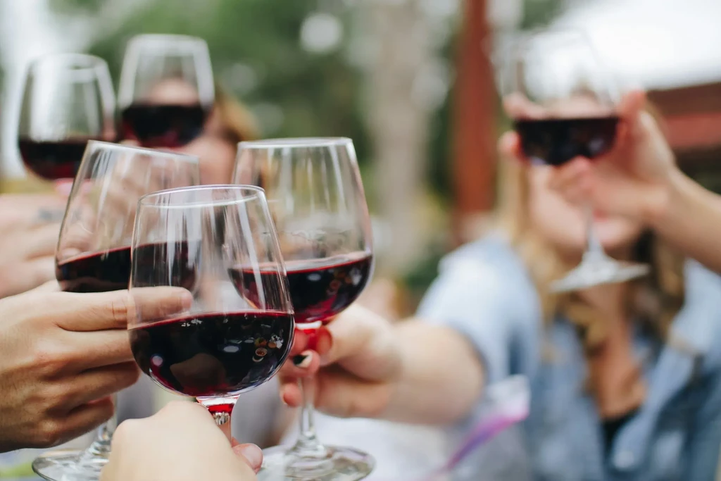 Multiple hands clinking red wine glasses together in a group toast.