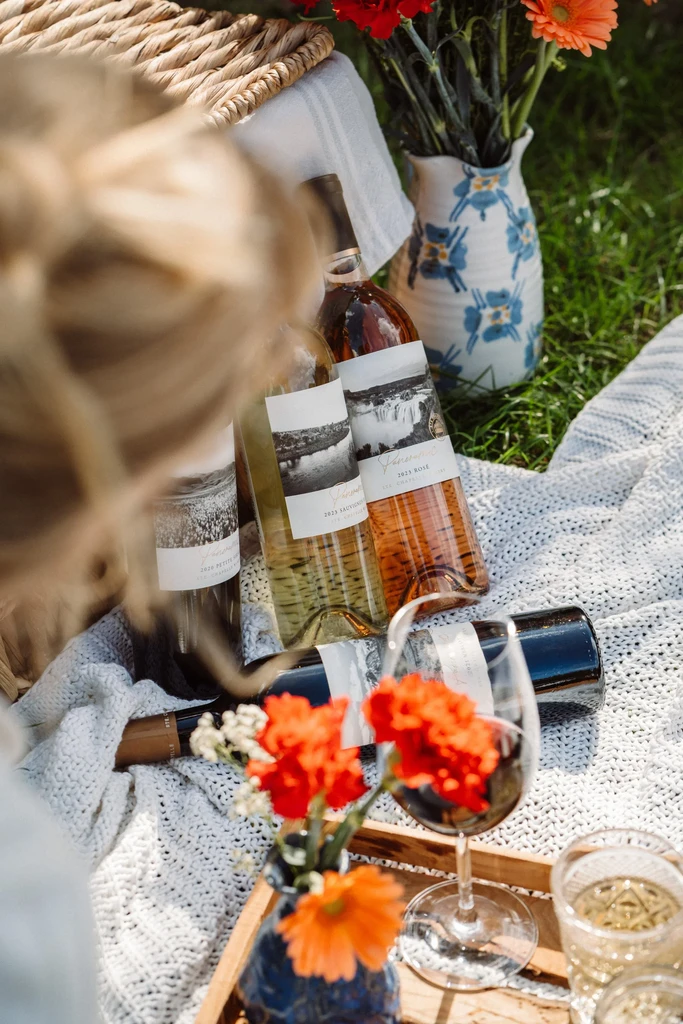 Outdoor picnic with wine bottles, glasses, and colorful flowers.