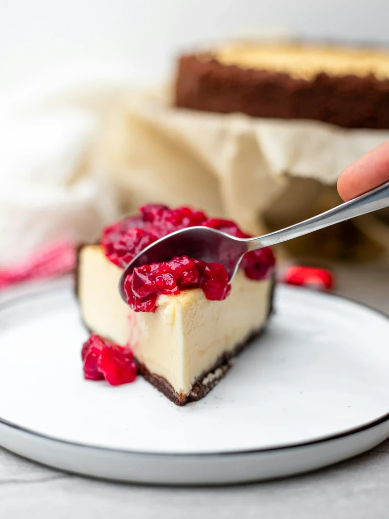 Cheesecake slice with raspberry compote, a spoon poised to scoop.