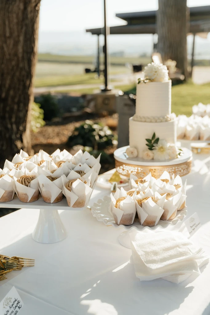 Outdoor dessert display with cupcakes, white cake, golden forks.