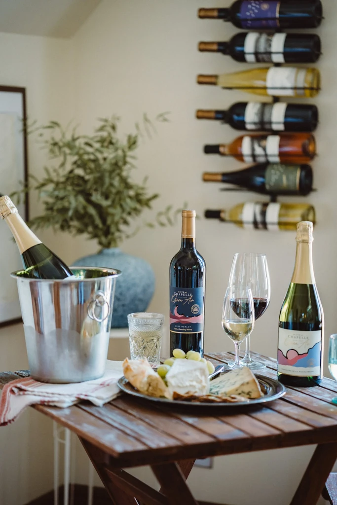 Wines, cheese board, and grapes on a wooden table, background wine rack.