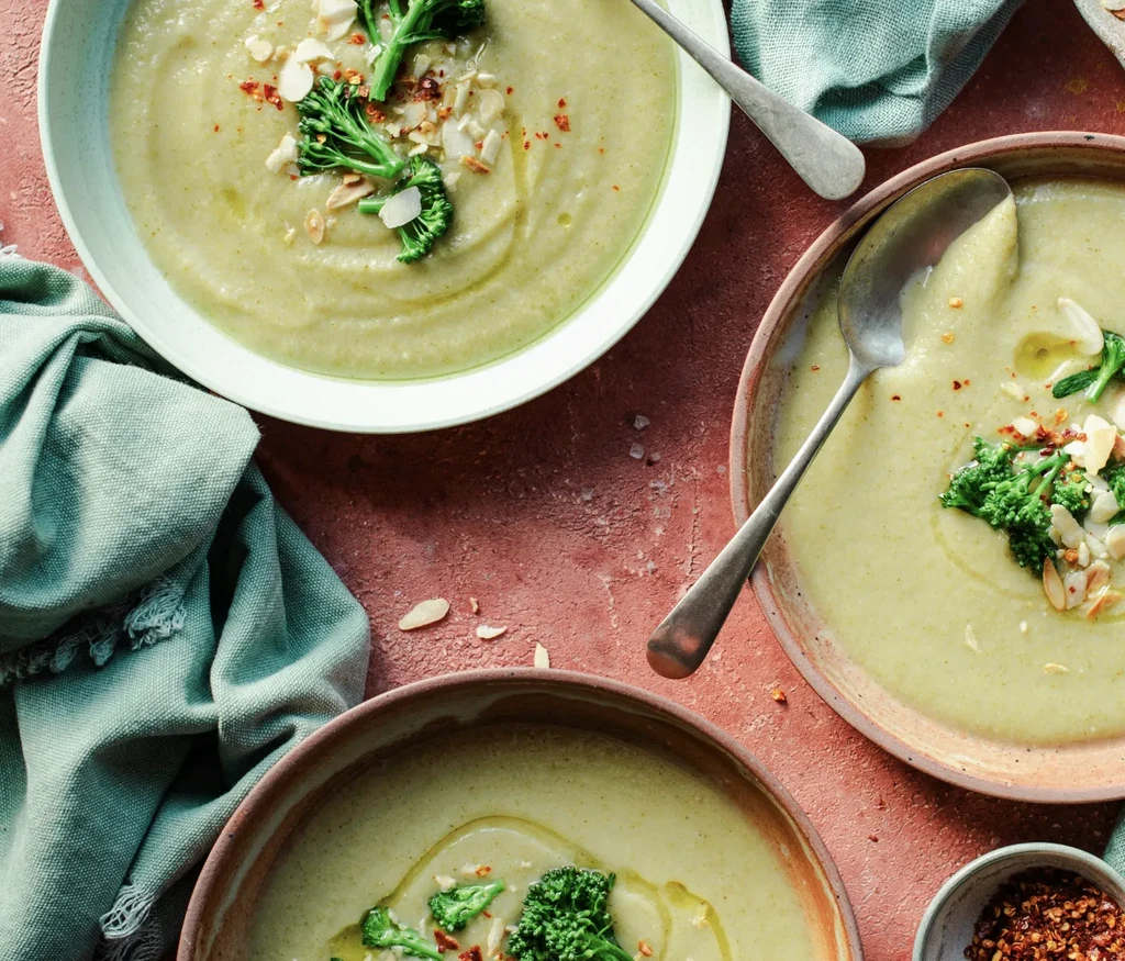 Three bowls of creamy light green soup, garnished with broccoli and almonds.