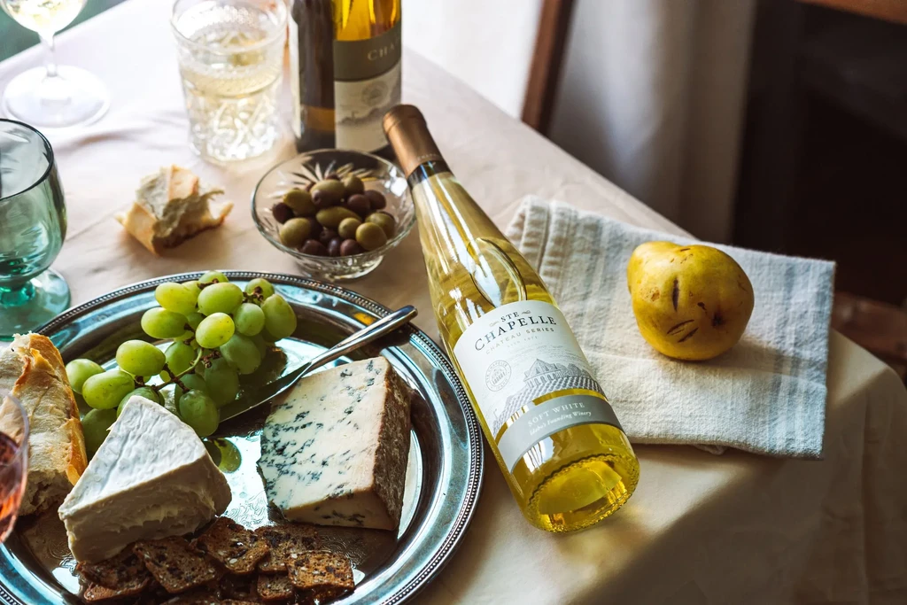Cheese and cracker platter with white wine, grapes, olives, and pear.