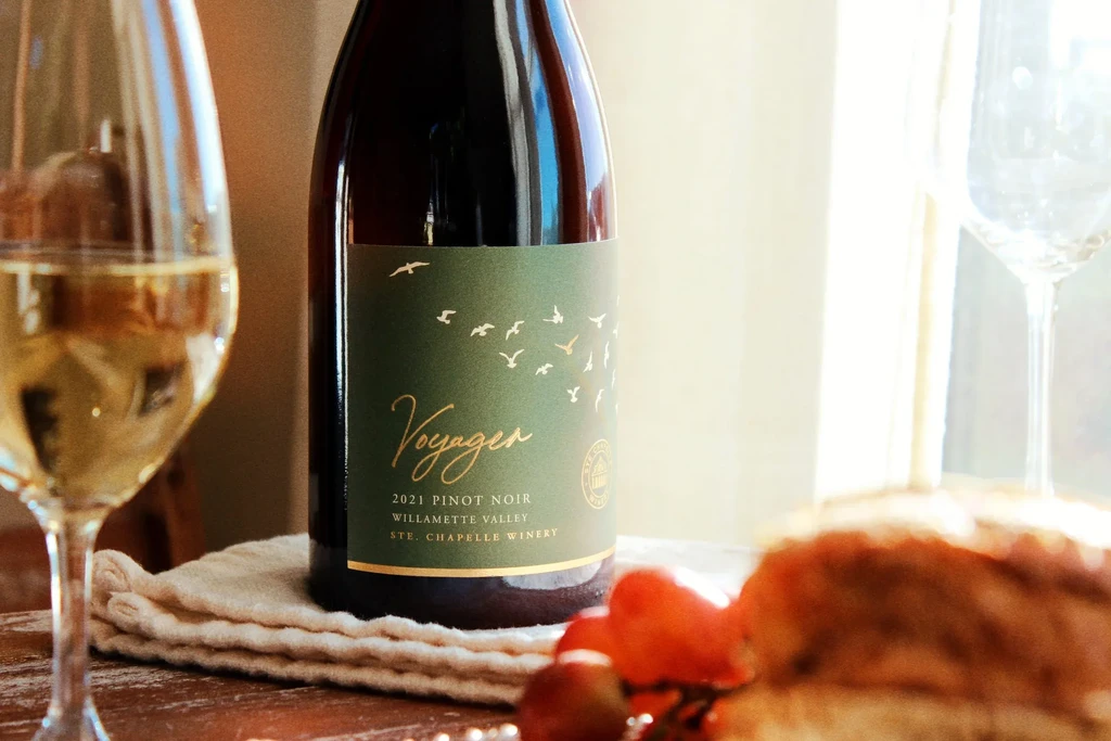 Close-up: Voyager 2021 Pinot Noir bottle, two glasses, grapes, bread.