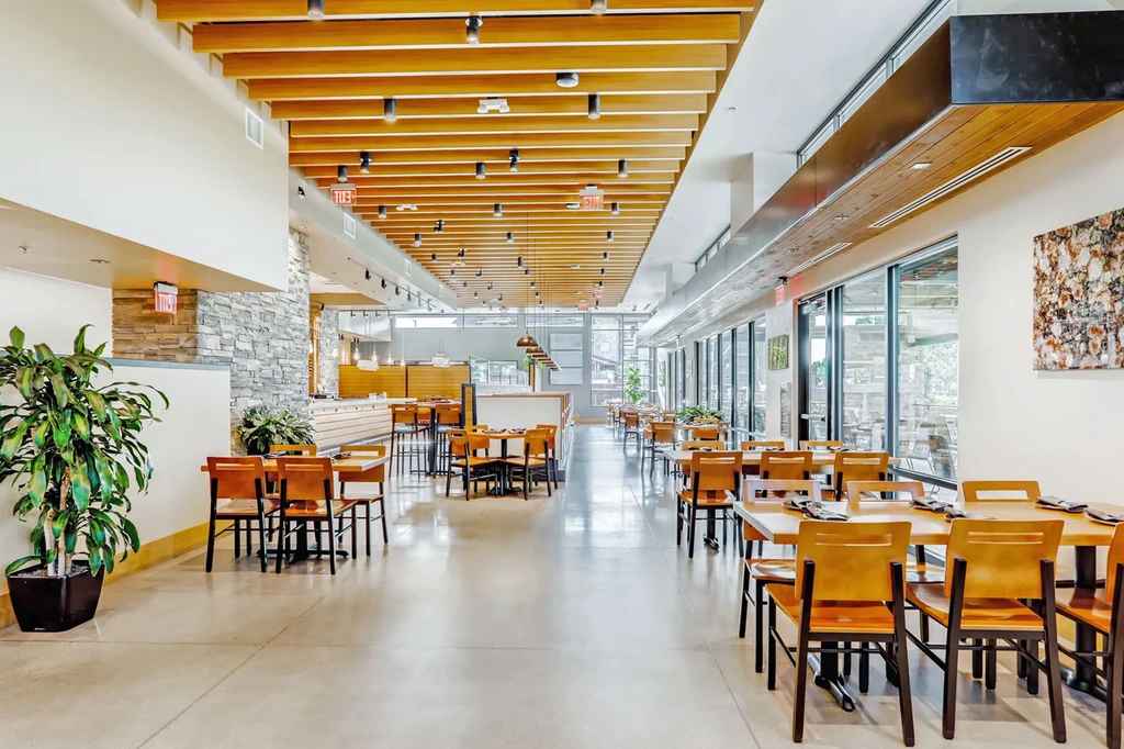Empty, modern restaurant interior with wooden beams, varied seating, and patio view.
