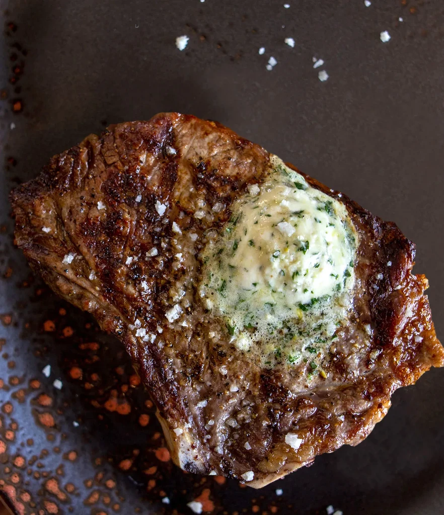 Seared steak with grill marks, sea salt, and melting herb butter.