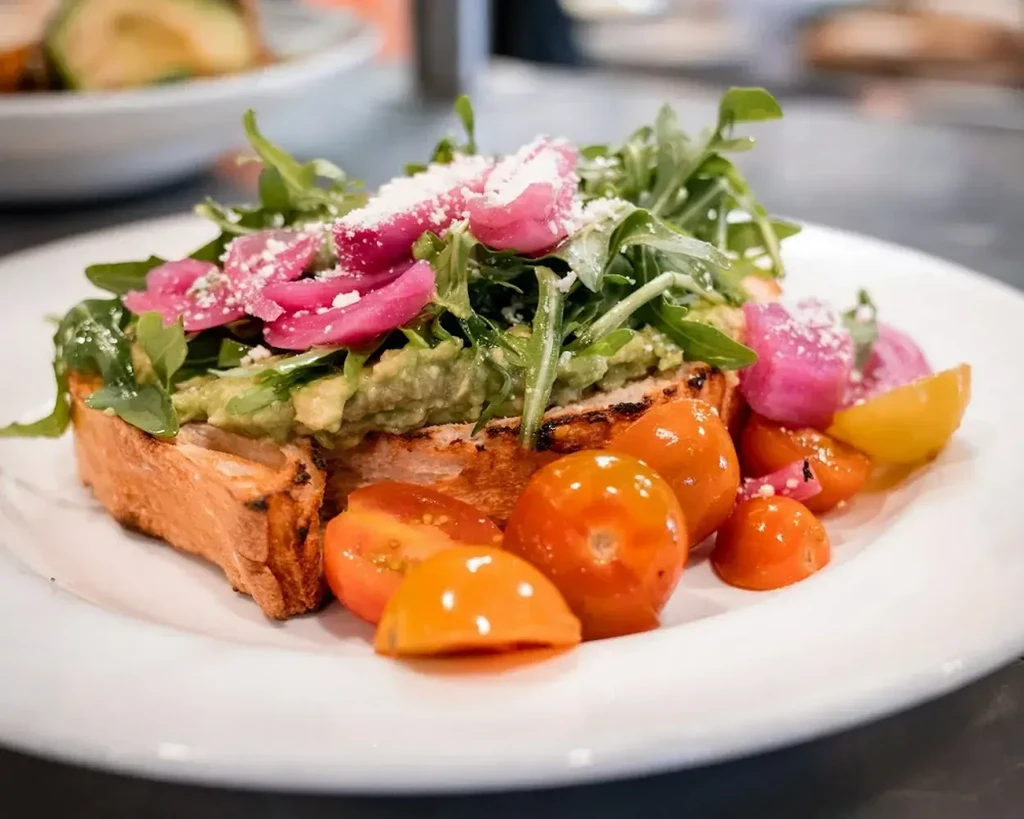 Avocado toast with arugula, pickled onions, and colorful cherry tomatoes.