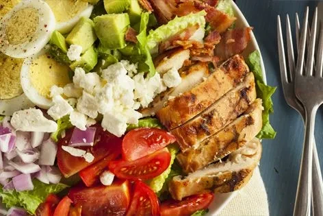 Vibrant composed salad with grilled chicken, avocado, bacon, and eggs.