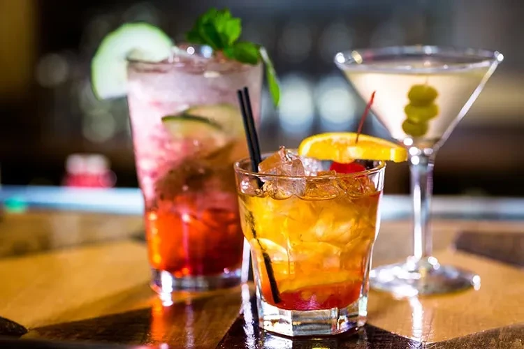 Three different cocktails: a pink highball, an orange rocks, and a yellow martini.