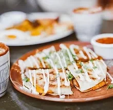 Quesadilla wedges with white sauce, green herbs, and red salsa.