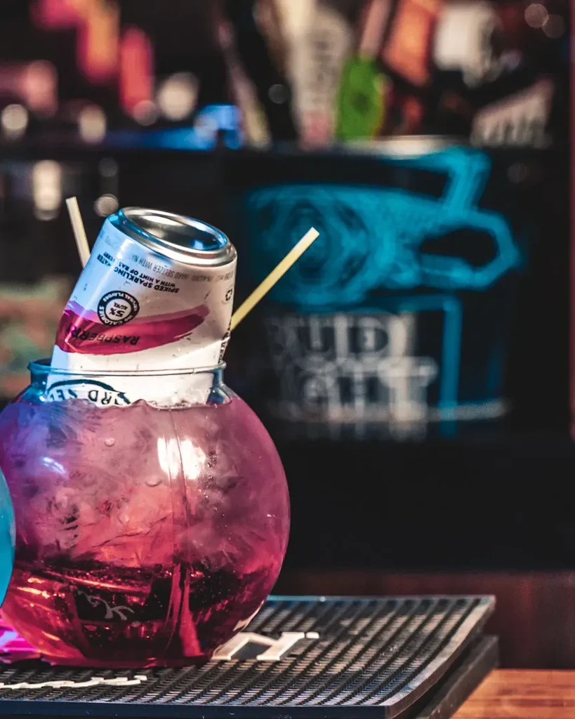 Spherical glass of pink drink with ice and a submerged RASPBERRY can.