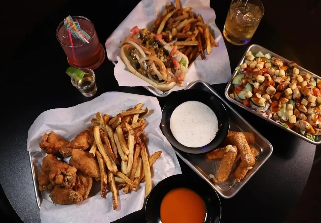 Top-down view of casual food: chicken wings, sandwich, salad, and drinks.