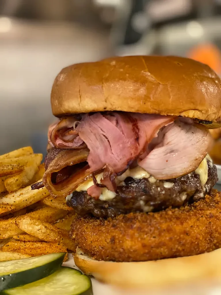 A large, multi-layered burger with fries and pickle slices.