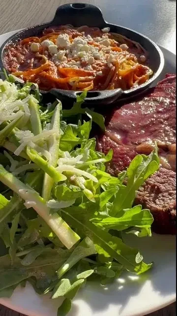 Pasta skillet, green salad with cheese, and cooked steak on a plate.