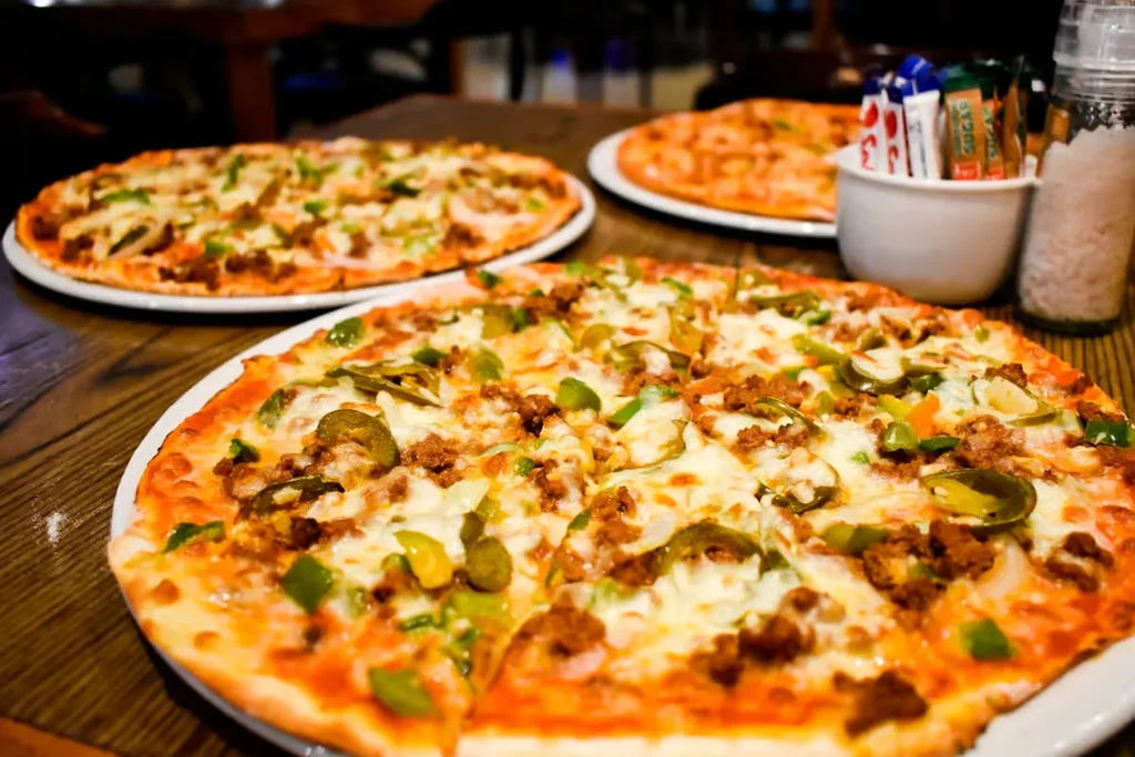 Several pizzas with meat, cheese, peppers on a dark wooden table.