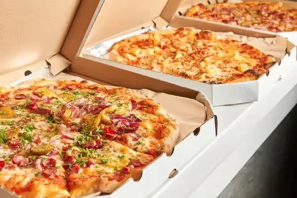 Three opened pizza boxes, showing supreme, Hawaiian, and mixed toppings.