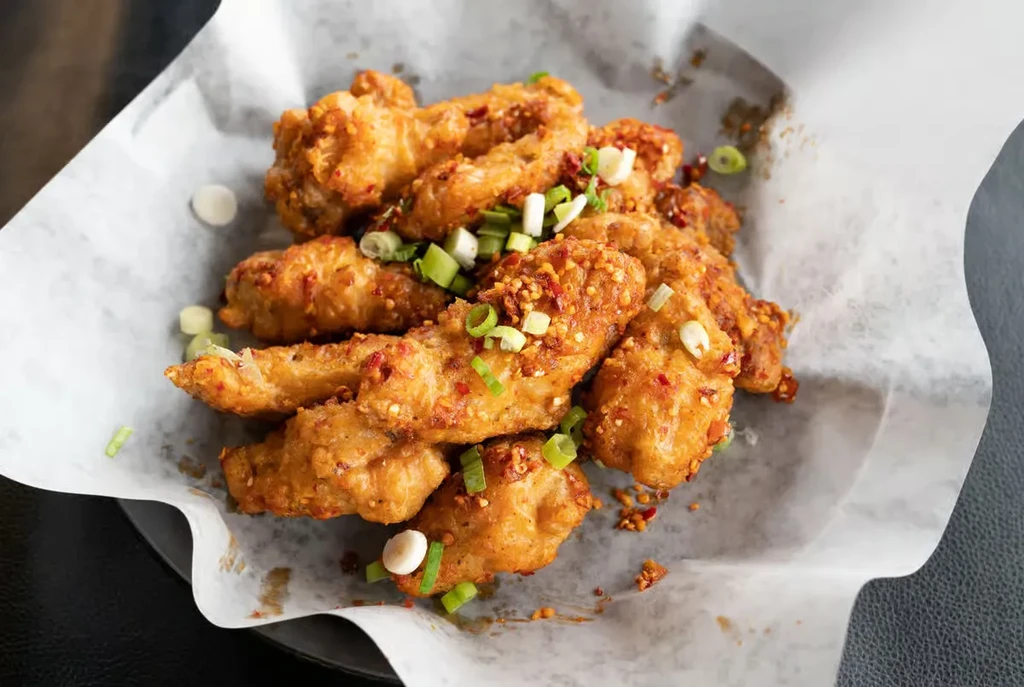 Golden fried chicken in a basket, with red pepper and green onions.
