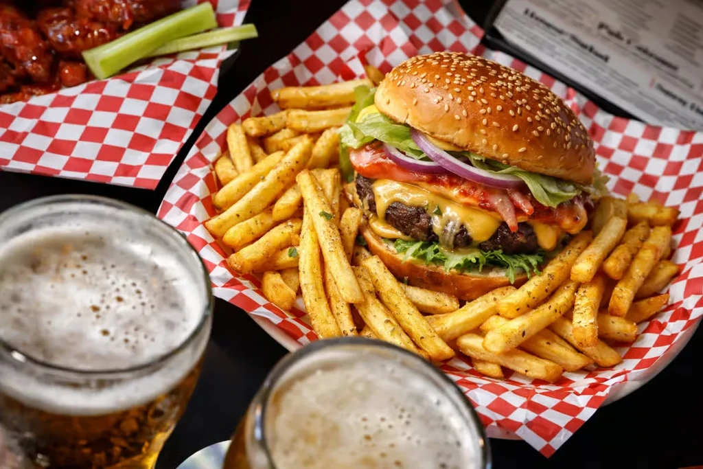 High-angle view: cheeseburger, fries, beer, and chicken wings in a bar.