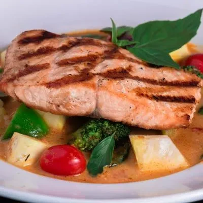 Grilled salmon with broccoli, root vegetables, tomatoes, and creamy sauce.