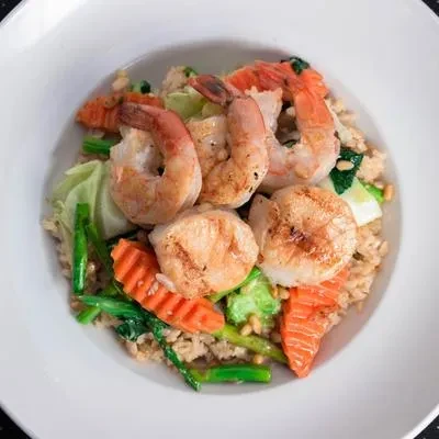 White bowl with seared shrimp, scallops, and colorful vegetables on rice.
